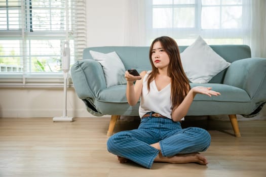 Unhappy young woman watch movie on television at home, bored beautiful female holding tv remote control sitting floor of sofa in living room at home, boring with television program