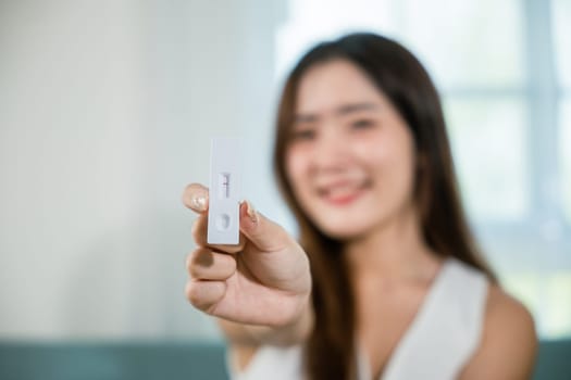 Close up woman showing rapid antigen test kit for selftest with Negative result during swab COVID-19 testing, female holding perform fast coronavirus ATK self test at home in living room, nasal