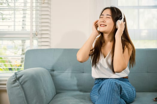 Woman wear earphone listen music application on smartphone, Asian young female wearing headphones listening to music with smart mobile phone and relaxing while sitting on sofa in living room at home
