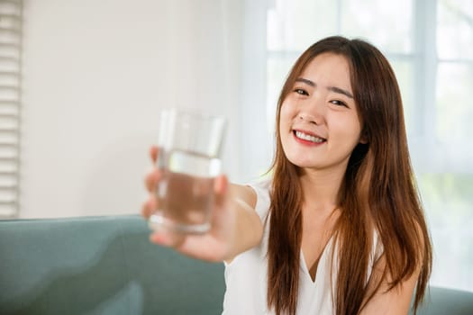 Happy smiling female beauty with water glass for drink in living room, Portrait of Asian young woman holding drinking nature water on hand at home, Healthy lifestyle
