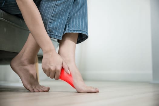Asian beautiful female problems with foot at home, painful ankle injury, Young woman sitting on sofa holding her feet and stretch muscles have symptoms feeling pain, Health care and medical concept