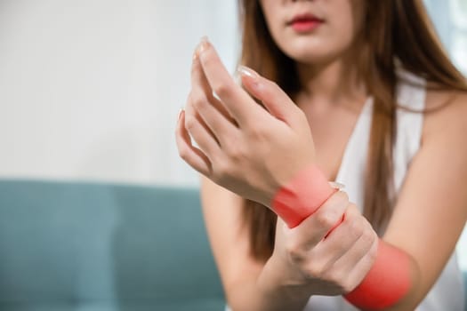 Closeup hand. Asian woman hand problem injury feeling joint pain, young female sitting on sofa holds suffering her wrist at home, performing self-massage, Health care and medical concept