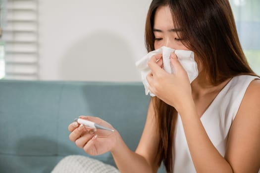 Sick woman have symptom sick high fever she checking her temperature with thermometer in living room at home, young female suffering from flu cold and fever, health care and medical concept