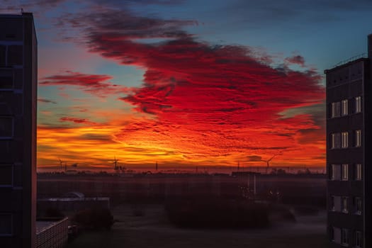 Sunset with golden twilight and illuminating clouds in the sky, with silhouette of tree and vegetation.Fantastically illuminated cloud at dawn in yellow-orange-red tones. View from the window.