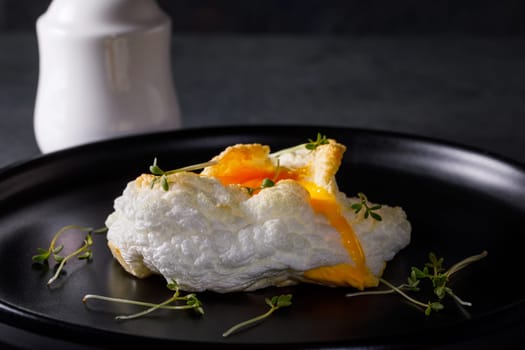 Tender baked egg. Orsini eggs in a cloud. French breakfast on a dark dish with a white salt shaker.