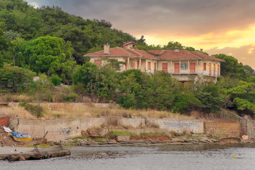 View of old abandoned house at the mountains of Kinaliada island from Marmara Sea, with dense big trees in the background, at sunrise, Istanbul, Turkey