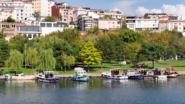 Istanbul, Turkey - September 1, 2022: Boats docked at the coast of the Golden Horn, with background of green park with dense big trees, and residential houses, in a sunny summer day