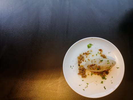 Lithuanian national dish zeppelins or Cepelinai or cepelins or didzkukuliai with fried bacon and herbs on white plate on black table