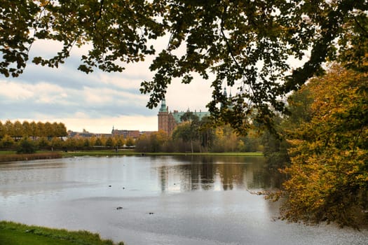 Frederiksborg Castle Park in autumn with mighty deciduous trees on the garden meadows and landscaped lake. Colorful colors of the leaves. Walk in Denmark