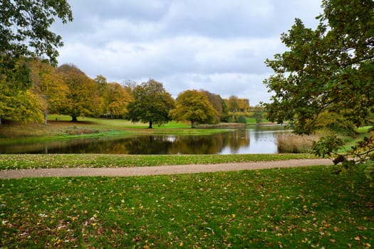 Frederiksborg Castle Park in autumn with mighty deciduous trees on the garden meadows and landscaped lake. Colorful colors of the leaves. Walk in Denmark