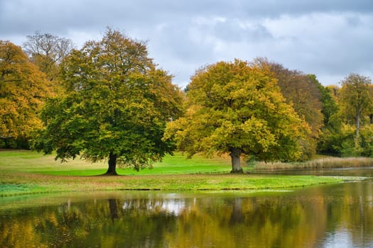 Frederiksborg Castle Park in autumn with mighty deciduous trees they are reflected in the created lake. Bright colors of the leaves. Walk in Denmark