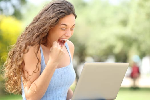 Excited woman celebrating success with a laptop in a park