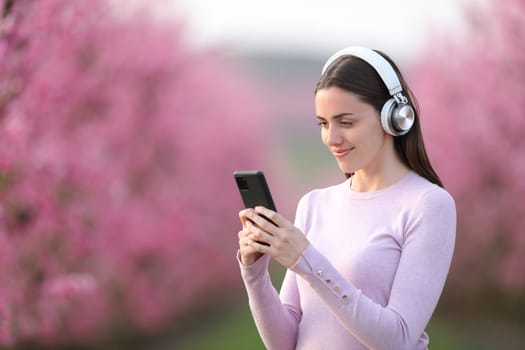 Woman listening to music in a pink field with phone and headphones