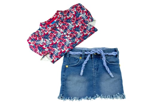Children clothes. Fashionable short jeans skirt with blue white linen twine for little girl and a folded shirt with floral print isolated on a white background.Kids colorful summer fashion.