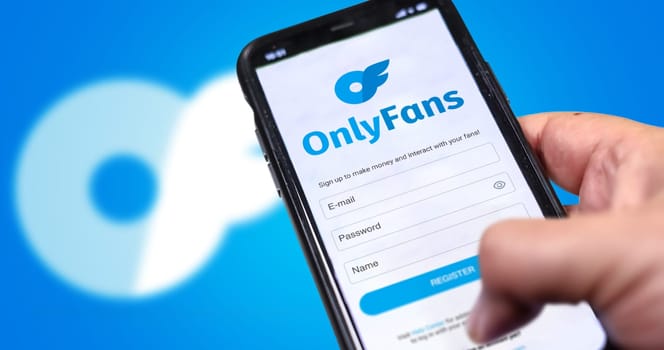 London, UK, August 2021  a hand holds a mobile phone with the OnlyFans registration form on the screen and the logo blurred in the background. OnlyFans is an internet content subscription service