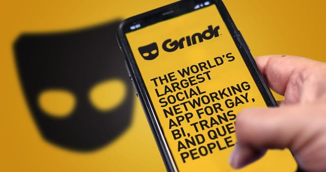 San Francisco, CA, US, May 2022: hand holding a phone with Grindr mobile application on screen. In background the Grindr logo blurred. Grindr is dating application for gay, bi, trans, and queer people