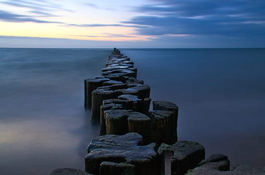 Groynes protruding into the horizon in the Baltic Sea. Long exposure with muted colors. Landscape shot by the sea