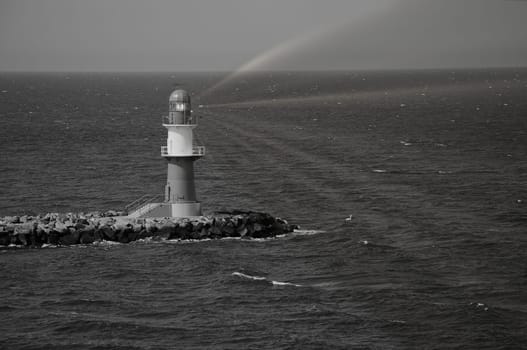 black and white photo of the lighthouse on the Warnow River in Rostock on the Baltic Sea. Landmark of the city. Waves on the stone edge. Landscape photo from Germany