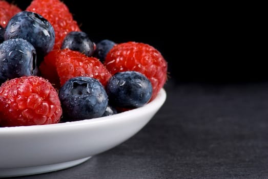 Plate of fresh blueberries and raspberries on balck background