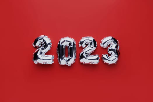 Christmas or New Year background. Red color flat lay with silver shiny 2023 balloon numbers in the center. Simple minimalistic greeting card.