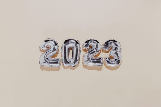 Christmas or New Year background. Beige color flat lay with silver shiny 2023 balloon numbers in the center. Simple minimalistic greeting card.