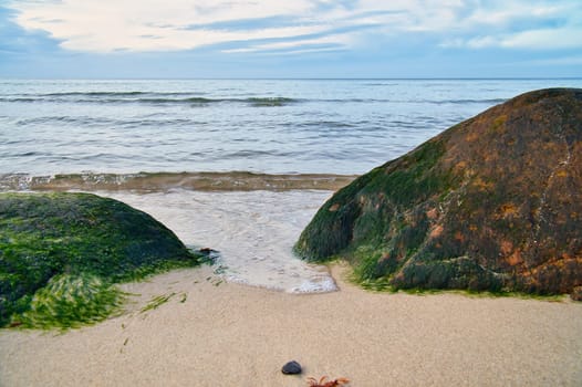 Big stone on the sandy beach in front of the sea with clouds in the sky. Denmark in Scandinavia. Landscape shot from nature in the north