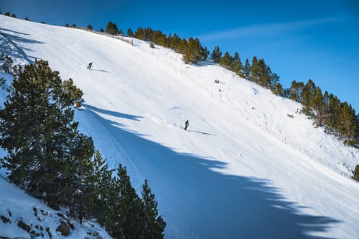 Couple of skiers skiing fast on steep piste or ski slope in Pyrenees Mountains. Winter ski holidays in El Tarter, Grandvalira, Andorra