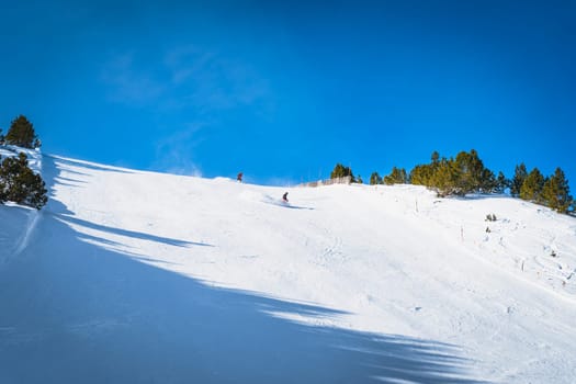 Couple of skiers having fun and going fast on steep piste or ski slope in Pyrenees Mountains. Winter ski holidays in El Tarter, Grandvalira, Andorra