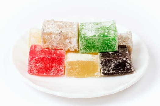 Colorful Turkish delight blocks with different tastes are on white plate on white background.