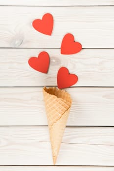 Vertical shot of hearts moving from waffle cone like confetti on light wooden background. Ice cream dessert and other sweets as present on saint Valentine's Day. Love and romance. Copy space, flat lay