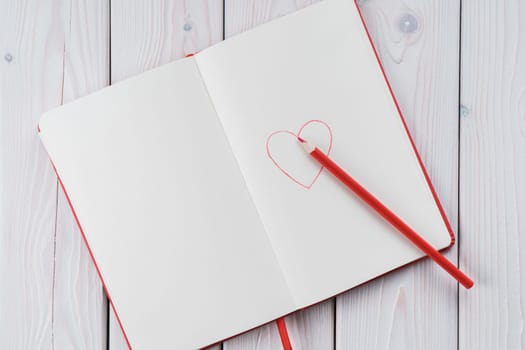Red diary notebook with white papers, craft pencil and red drawing heart on page. Love letter message for beloved people, love feelings for saint Valentine Day or woman day. Copy space, top view
