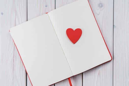 Red diary notebook with white papers, craft red paper heart on page. Love letter message for beloved people, confession and feelings for saint Valentine's Day or woman day. Copy space, top view