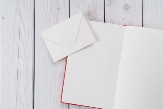 Red diary book with white paper with handmade, craft envelope on light wooden desk background. Traditional message letters sending, postal cards for business and lifestyle. Copy space, flat lay