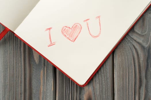 Red diary book with white paper with sign label I love you in the corner of page with red shaded line heart. Love letter message for beloved, confession and feelings for Valentines Day. Top view