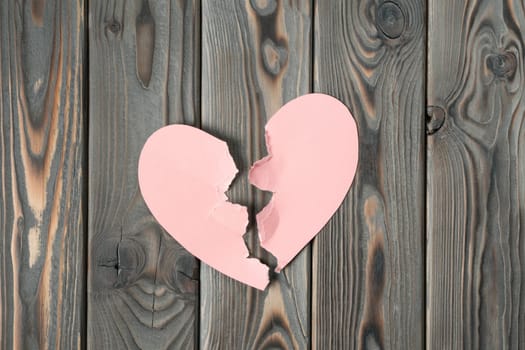 Pink torn paper heart halves laying together on dark wooden table. Broken heart, breaking up, past relationship and rejection on saint valentines day. Unspoken feelings. Top view, copy space, flat lay