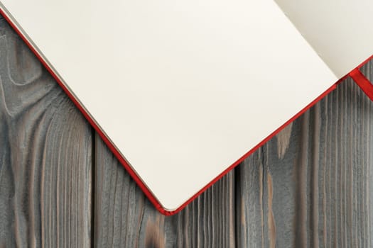 Red diary, notebook corner of white paper pages on dark wooden background. Making notes in empty workbook on office desk. Personal organizer as reminder. Blank and template. Copy space, top view