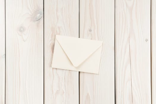 White craft handmade closed paper envelope laying on white wooden plank background. Post card message, letter sending. New delivery and retro traditional invitation. Copy space, mockup, flat lay