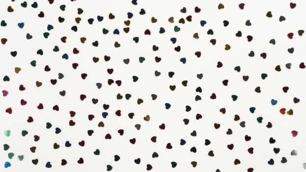Small colorful paper foil hearts on white background. Decorative foil and paper elements for art design. Glowing and shining art composition. Saint valentines day. Full frame, wallpaper, top view