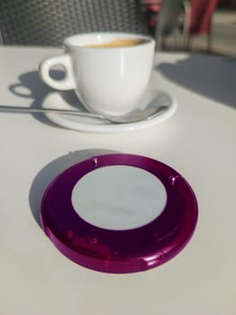 Coaster pager device close to coffee cup at terrace. Wireless communications device for restaurant costumers