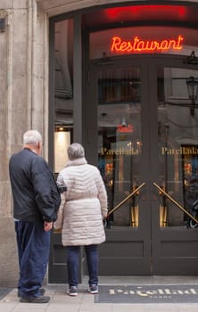 Barcelona, Spain - Dec 29th 2019: Elderly couple of tourists reading Parellada restaurant menu. Gothic Quarter, Catalonia, Spain