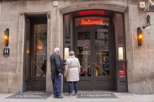 Barcelona, Spain - Dec 29th 2019: Elderly couple of tourists reading Parellada restaurant menu. Gothic Quarter, Catalonia, Spain
