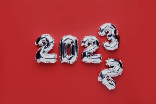 Christmas or New Year background. Red color flat lay with silver shiny 2023 balloon numbers in the center. Simple minimalistic greeting card.