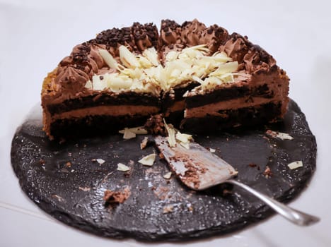A cut chocolate cream cake with pieces already missing.