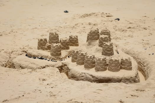 A big sandcastle built on the beach with buckets and ramekins.