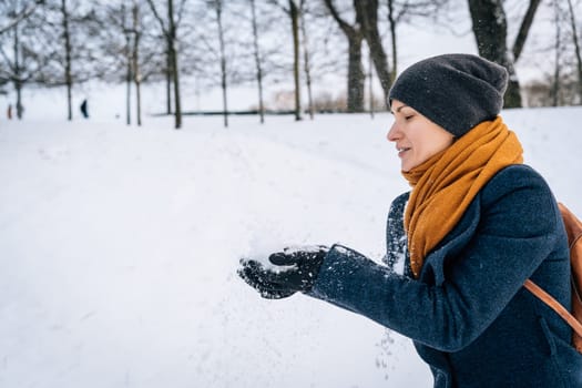 A woman in warm clothes throws snow with her hands.