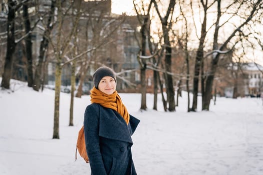 A woman in warm winter clothes looks into the camera and smiles in winter.
