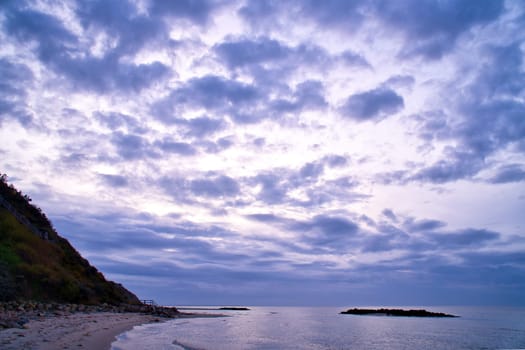 Sunset on the Danish coast. Beach, waves. Hill with trees in background. Landscape photo from sea
