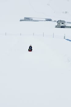 Mom and baby enjoy a sleigh ride. Sledding for children. Child riding a sleigh. Children play outdoors in the snow. Outdoor fun for family Christmas holidays.