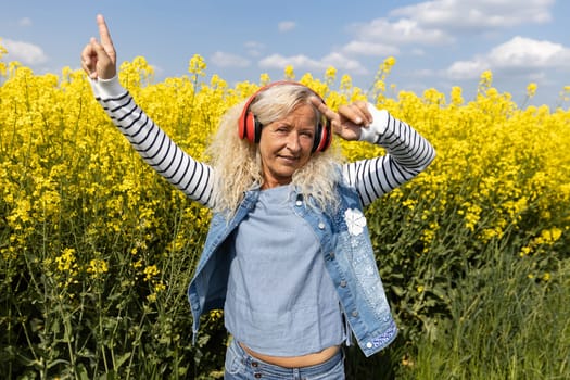 Elderly Woman listen to music with headphones in blooming canola field