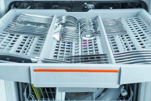 Upper pullout shelf of dishwasher with clean sparkle cutlery in partitions. Dish washing, spoons, forks and knives, modern household appliance. Silverware cleaning. Convenient kitchen equipment.